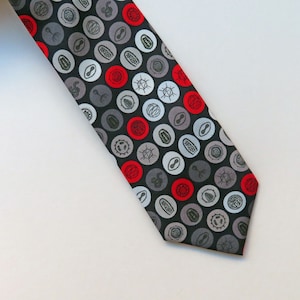 May include: A black necktie with a repeating pattern of red, white and grey circles. Each circle features a different design, including a small, stylised image of a seed or plant.