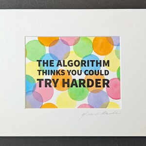May include: A matted print featuring the black text THE ALGORITHM THINKS YOU COULD TRY HARDER centered over a background of overlapping translucent watercolor circles in shades of pink, yellow, orange, green, blue, and purple on white paper.