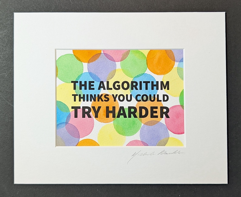 May include: A matted print featuring the black text THE ALGORITHM THINKS YOU COULD TRY HARDER centered over a background of overlapping translucent watercolor circles in shades of pink, yellow, orange, green, blue, and purple on white paper.