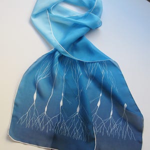 May include: A blue silk scarf with a white design of stylized neurons. The scarf is ombre, fading from a light blue to a dark blue.