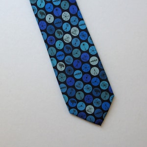 May include: A blue necktie with a pattern of blue and teal circles, each containing a black illustration of a neuron. The tie is made of a smooth fabric and is angled across a white background.