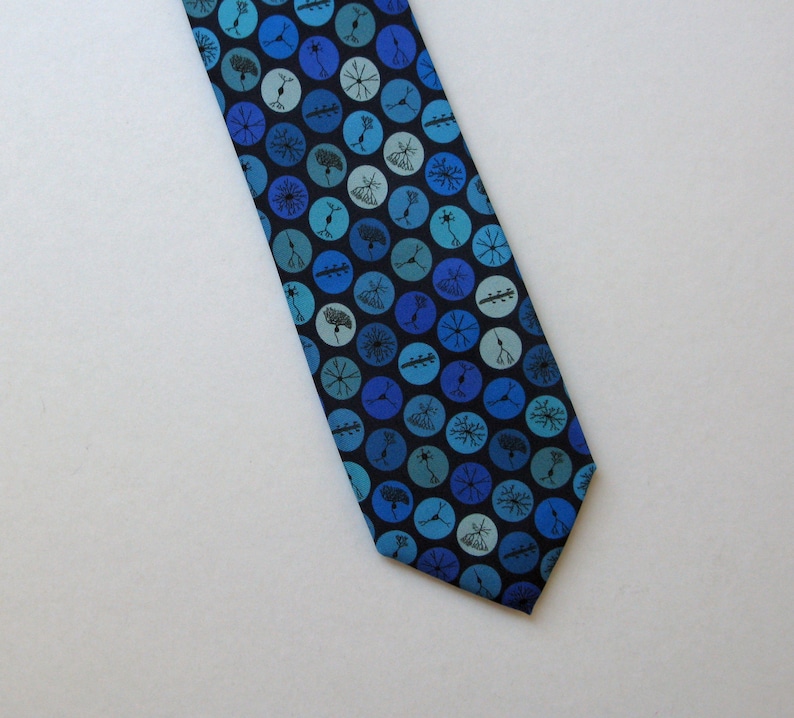 May include: A blue necktie with a pattern of blue and teal circles, each containing a black illustration of a neuron. The tie is made of a smooth fabric and is angled across a white background.