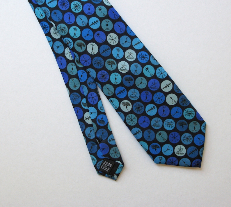 May include: A blue silk tie with a repeating pattern of blue and teal circles on a black background. Each circle contains a unique, abstract design. The tie is angled across a white surface, showcasing its design and texture.