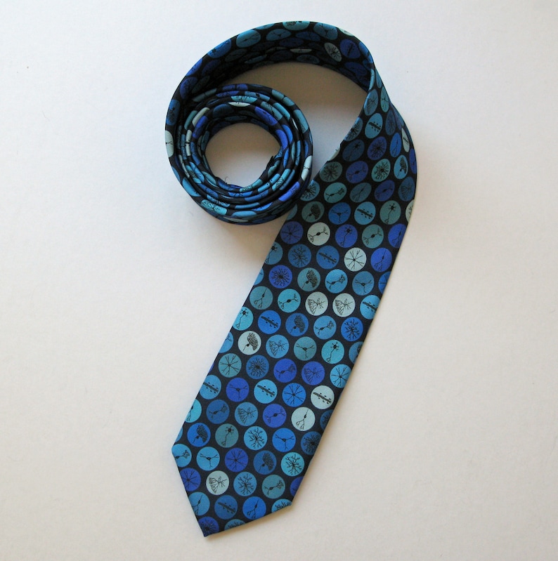 May include: A rolled-up necktie with a pattern of blue circles and white floral designs on a dark blue background. The tie is made of a smooth fabric and is displayed on a white surface. The tie is a classic accessory.