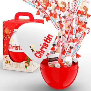 Könnte beinhalten: Eine rot-weiße Geschenkbox zum Thema Weihnachten mit einem großen eiförmigen Behälter. Das Ei ist geöffnet und zeigt eine Auswahl an Süßigkeiten, Pralinen und ein Glas Nutella. Der Name "Christin" steht auf dem Ei.