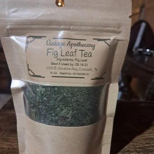 May include: A package of Vintage Apothecary Fig Leaf Tea. The tea is visible through a clear window in the bag. The label includes the ingredients, best-by date, and address. The bag is made of a light brown paper material.