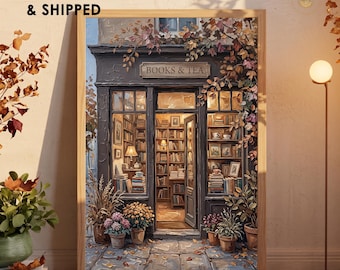 May include: A framed wall art print titled BOOKS & TEA depicting a storefront with large windows filled with bookshelves, warm interior lighting, and potted flowers on the sidewalk. The scene features autumn foliage and a textured, painterly style.