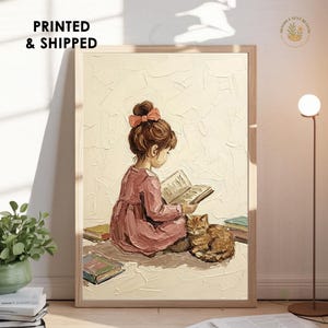 Puede incluir: Una lámina de arte enmarcada con una pintura al óleo texturizada de un niño con un lazo rosa en el pelo y un vestido rosa empolvado, sentado leyendo un libro abierto junto a un gato atigrado naranja dormido, rodeado de varios libros apilados.