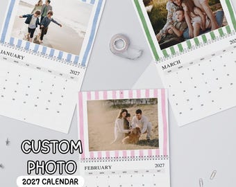 May include: Three custom photo wall calendars for 2027 with spiral binding. Each calendar features a unique family photograph at the top, framed by vertical stripes in blue, green, or pink. The text CUSTOM PHOTO 2027 CALENDAR is visible.