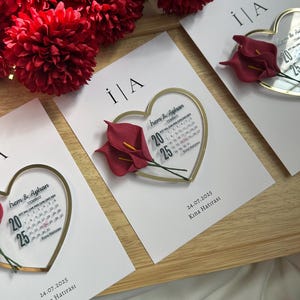 May include: White cards with gold heart-shaped frames and red calla lily accents. Each card features a calendar with the date 20-25 highlighted, and the text "İrem & Ayhan" and "24.07.2025 Kına Hatırası".