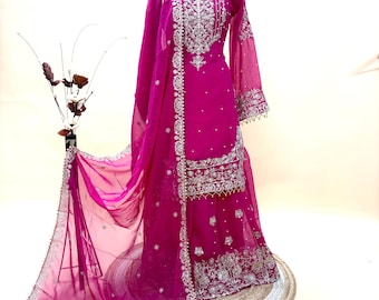 Op de afbeelding: Een levendige fuchsia-kleurige formele jurk met ingewikkelde zilveren borduursels. De jurk heeft een top met lange mouwen en een zwierige rok, aangevuld met een bijpassende doorschijnende sjaal. De halslijn is versierd met delicate versieringen.
