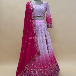 May include: A pink and fuchsia ombre lehenga choli set. The set includes a long skirt, a cropped top with long sleeves, and a matching dupatta. The skirt and top are embellished with silver embroidery. The dupatta is a solid fuchsia color.