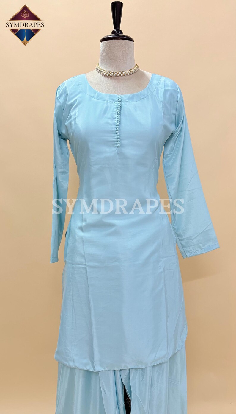 May include: Light blue Kurti and palazzo set. The long-sleeved Kurti features a round neckline and a buttoned placket. The palazzo pants are wide-legged. The text "SYMDRARES" is visible on the Kurti. The outfit is displayed on a mannequin.