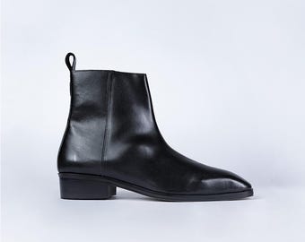 May include: A black leather ankle boot with a low heel. The boot features a pointed toe and a pull tab at the back. The smooth leather has a slight sheen. The boot is a classic style, suitable for various outfits.