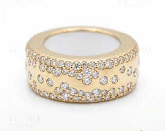 May include: A wide, gold-colored ring with a band of small, sparkling diamonds. The ring has a thick band with a series of diamonds set in a pattern around the outer surface. The inside of the ring is white. The ring is from Veyora Carats.