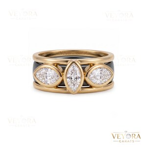 May include: A gold ring featuring three marquise-cut clear stones set horizontally in a row. The band has a black inner layer visible between the gold edges. The text Veyora Carats is engraved on the inner band and appears as a watermark.