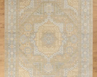 May include: A rectangular area rug with an intricate, symmetrical pattern in shades of beige, light blue, and muted green. The rug's design features a central medallion and repeating geometric motifs, creating a traditional aesthetic. The rug measures 9ft x 12ft.
