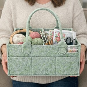 May include: A light green felt craft organizer with a handle, filled with yarn, embroidery hoop, needles, scissors, and other craft supplies. The organizer has multiple compartments and pockets for storage.