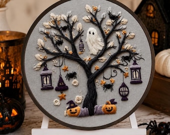 May include: A circular embroidery hoop featuring a hand-stitched design on grey fabric. The artwork depicts a dark tree with a white ghost, black spiders, purple lanterns, a witch hat, orange stars, and two jack-o'-lanterns at the base.