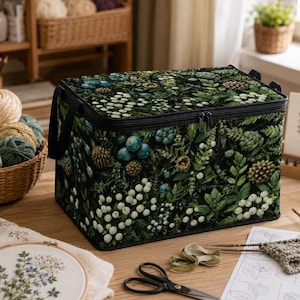 Puede incluir: Una bolsa de almacenamiento rectangular con base negra y un estampado botánico de helechos verdes, piñas y racimos de bayas blancas y azules. La bolsa cuenta con una tapa con cremallera, asas de tela negra y una forma estructurada.