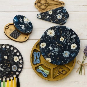 Könnte beinhalten: Eine Sammlung von Näh- und Stickwerkzeugen und -zubehör. Enthält Holz-Garnorganisatoren, Scherenetuis und einen Nadelhalter. Die Artikel weisen ein marineblaues Blumenmuster mit weißen und blauen Blumen und einem Kranichdesign auf.