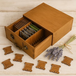 Op de afbeelding: Een houten theedoos met een lade, met theezakjes. De doos is open en onthult compartimenten voor theezakjes. Verschillende houten spoelvormige onderzetters liggen verspreid rond de doos. Een bosje lavendel is met touw gebonden.