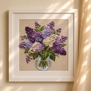 Op de afbeelding: Een ingelijst kunstwerk met een gedetailleerde borduursel van seringen in paarse en witte tinten. De bloemen zijn gerangschikt in een heldere glazen vaas met groene bladeren. Het kunstwerk is geplaatst tegen een neutrale achtergrond en in een witte lijst.