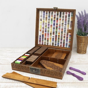 May include: A wooden craft organiser box with multiple compartments, filled with spools of colourful thread and wooden bobbins. The box is open, revealing a variety of colours and patterns. The box is decorated with carved floral designs.