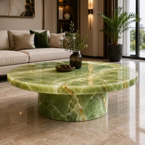 May include: A round coffee table crafted from polished green onyx stone with natural white and gold veining. The table features a thick circular top supported by a matching cylindrical pedestal base, showcasing a smooth, reflective surface finish.