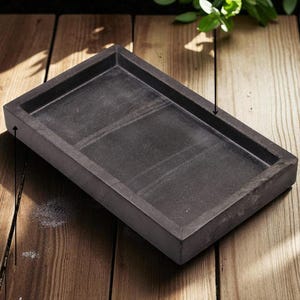 Könnte beinhalten: Ein rechteckiges, dunkelgraues Tablett mit glatter, matter Oberfläche und erhöhten Rändern. Das Tablett hat ein schlichtes Design mit flachem Boden und einheitlicher Farbgebung und bietet eine funktionale Ablagefläche für verschiedene kleine Gegenstände.
