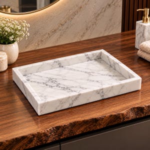 May include: A rectangular white marble tray featuring prominent grey veining throughout its surface. The tray has a flat base and raised edges, showcasing the natural stone pattern and polished finish of the material in a simple, functional design.