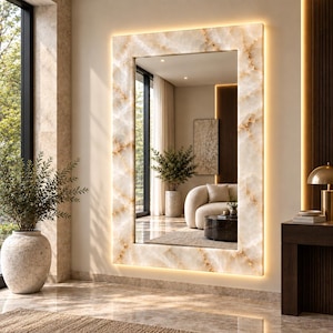 May include: A rectangular wall mirror featuring a thick frame with a cream and tan marble-like pattern. The frame is illuminated by integrated LED backlighting that casts a warm glow against the wall. The mirror reflects a room interior.