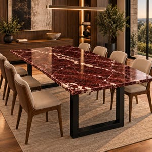 Puede incluir: Una mesa de comedor rectangular con un tablero de mármol rojo intenso pulido con vetas blancas prominentes, sostenida por una base de metal negro en forma de U. La mesa está rodeada por seis sillas con estructura de madera y asientos tapizados en beige claro.