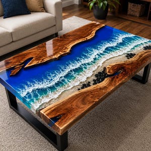 Puede incluir: Una mesa de centro rectangular con un tablero de madera de borde natural y una incrustación central de resina. La resina representa una escena oceánica azul con olas de espuma blanca, una textura de arena y piedras negras sobre metal.