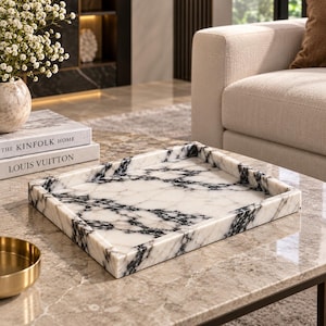 Peut inclure: Un plateau rectangulaire en marbre blanc présentant des veines noires marquées sur toute la surface et des bords surélevés. Le plateau possède une finition lisse et polie avec un motif constant de stries sombres sur la base en pierre blanche.
