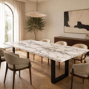 Peut inclure: Une table à manger rectangulaire avec un plateau en marbre blanc et gris et des pieds en métal noir, entourée de six chaises aux assises rembourrées beige clair et aux cadres en bois foncé, dans une pièce au sol en chevrons.