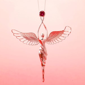 May include: A silver angel pendant necklace with a ruby gemstone at the top. The angel has outstretched wings and arms raised above its head. The pendant hangs from a delicate silver chain against a pink background.