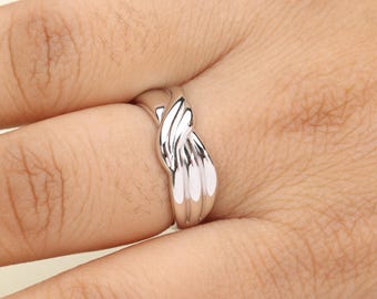 May include: A silver-colored ring with a braided design. The ring is smooth and shiny, reflecting light. The ring's design features a series of curved, overlapping bands, creating a textured appearance. The ring is worn on a finger.