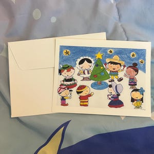 May include: A Christmas-themed greeting card with a hand-drawn illustration of children around a decorated Christmas tree. The card features a white envelope and is set against a blue and white patterned background.