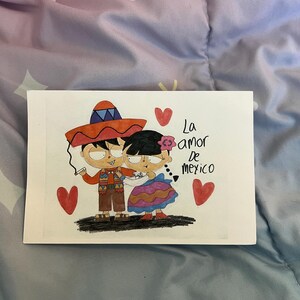 May include: A hand-drawn illustration on white paper depicts a couple in traditional Mexican attire. The man wears a sombrero and the woman has a flower in her hair. The text "La amor de Mexico" is written above them, with red hearts scattered around.