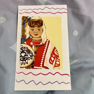 May include: A vibrant illustration on a white card depicts a person in traditional Native American dress. The person is wearing a red and white robe, a decorative headband, and holding a shield with black and white designs. The card has wavy pink and purple borders.