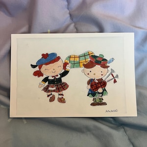 May include: A watercolor illustration of two cartoon figures in Scottish attire. One figure wears a blue hat and plaid skirt, the other plays bagpipes. The artwork is on a white card with the artist's signature.