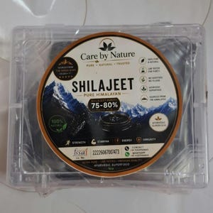 Può includere: Un contenitore rettangolare in plastica trasparente con un'etichetta circolare per Care by Nature Shilajeet. L'etichetta presenta un grafico di montagna, il testo Shilajeet Pure Himalayan, 75-80% acido fulvico e icone per forza, energia e immunità.