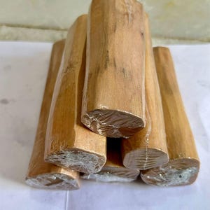 Pu&ograve; includere: Una collezione di tronchi di legno di sandalo marrone chiaro, avvolti in plastica trasparente. I tronchi sono impilati insieme, mostrando la loro venatura naturale e la loro forma. Le estremit&agrave; dei tronchi sono visibili, rivelando le loro superfici tagliate.