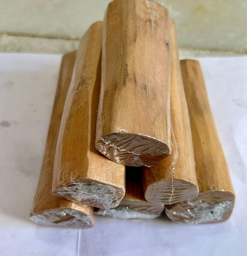 Pu&ograve; includere: Una collezione di tronchi di legno di sandalo marrone chiaro, avvolti in plastica trasparente. I tronchi sono impilati insieme, mostrando la loro venatura naturale e la loro forma. Le estremit&agrave; dei tronchi sono visibili, rivelando le loro superfici tagliate.