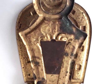 May include: Gold-toned metal paper clip shaped like a horseshoe with a decorative top. The clip has a small rectangular opening in the center.