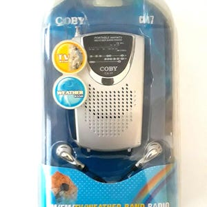 Peut inclure: Une radio portable AM/FM/TV/Météo Coby CX-17 argentée avec une antenne noire et des écouteurs noirs. La radio est emballée dans une boîte bleue et argentée avec un motif arc-en-ciel.