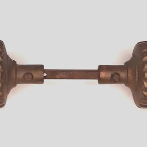 May include: Antique bronze door knob set. The set features two ribbed, rounded knobs joined by a rectangular rod. The knobs have a warm, aged bronze finish, indicative of vintage hardware. The design is simple and functional, suitable for a classic or vintage aesthetic.