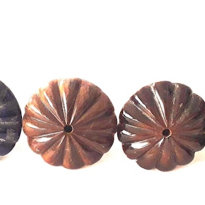 Puede incluir: Cuatro objetos decorativos tallados en forma de flor, en varios tonos de marrón y gris azulado. Cada uno tiene un agujero central. Los objetos están dispuestos en fila sobre un fondo blanco. Los objetos parecen ser de madera o piedra.