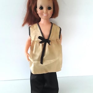 May include: A vintage doll with long, red hair wearing a gold sleeveless top with a black bow and black trousers.